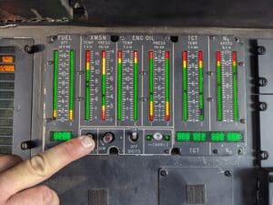 A hand is pointing to the green and red lights on an airplane control panel.